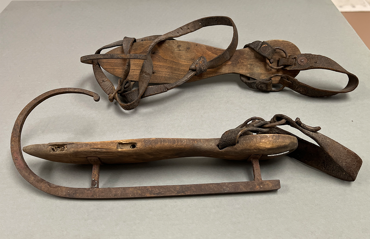 Ice skates with crude wood platforms, curled metal blades, and leather straps.