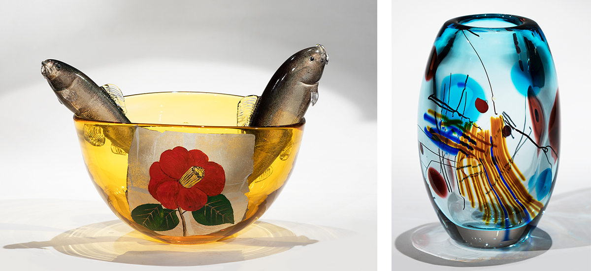 A yellow glass bowl with two glass fish rising out of the middle, and an abstractblue and yellow vase
