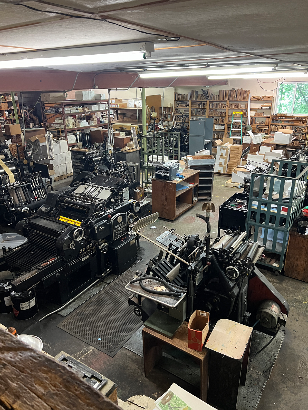 The Heidelberg presses (foreground) and handcarved linoleum blocks (back wall) used to print Gwen’s designs, 2024