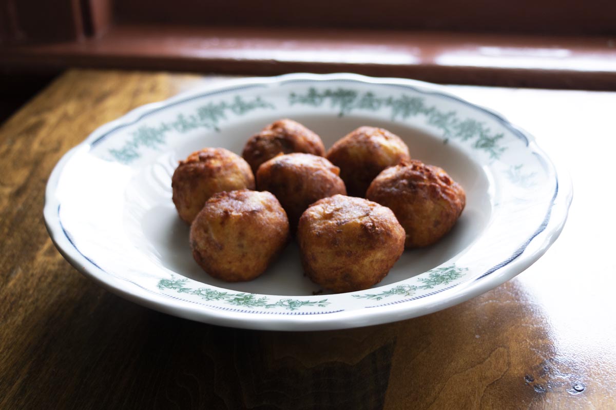 Shallow white bowl with green floral pattern around rim, filled with fried meatballs, sitting on wooden table