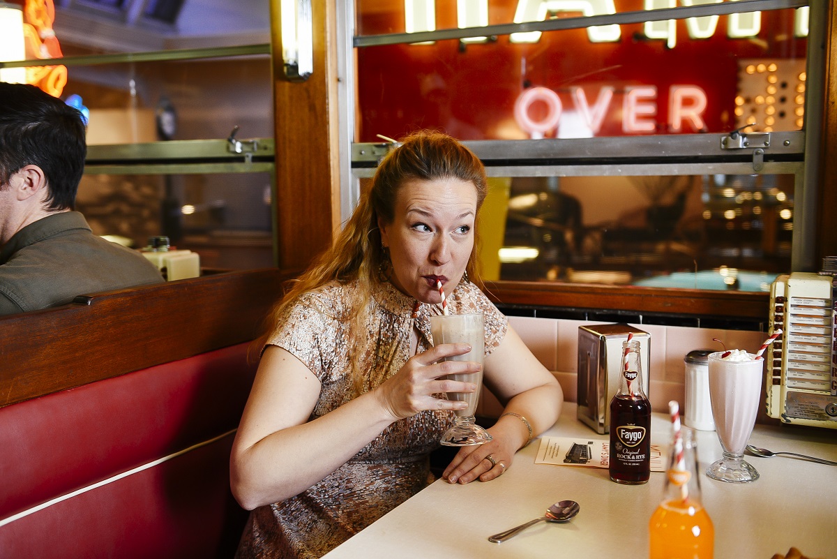 Woman sits in diner booth and sips a milkshake from a straw